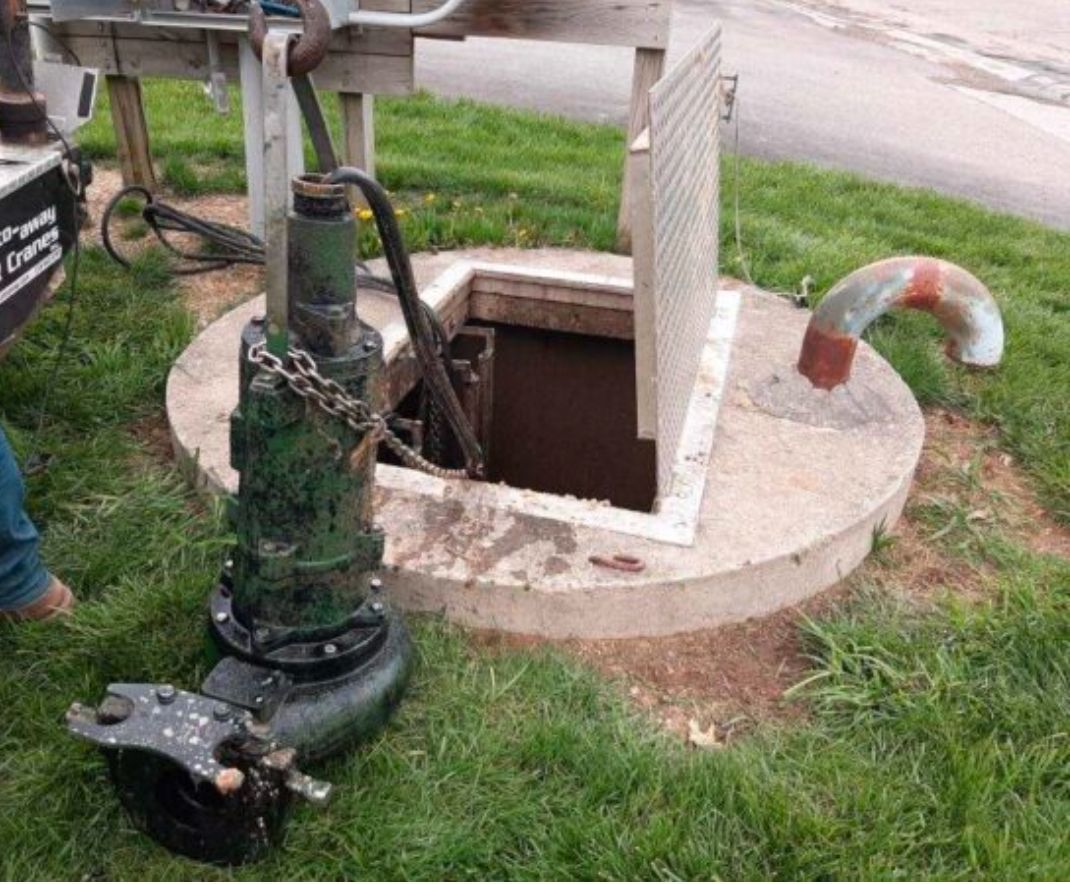 A green pump is sitting in the grass next to a manhole cover.