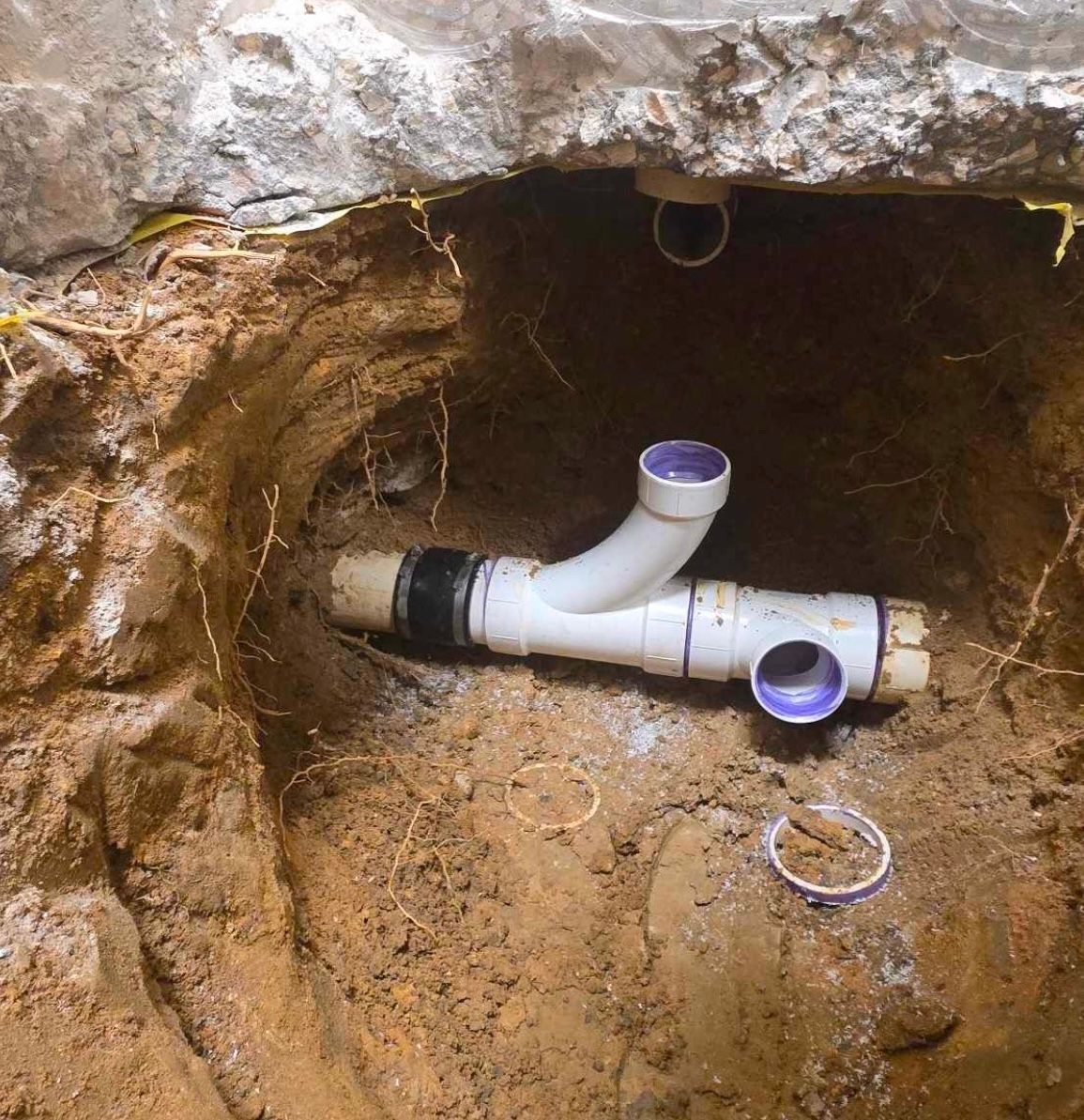 A white pipe is laying in the dirt in a hole.