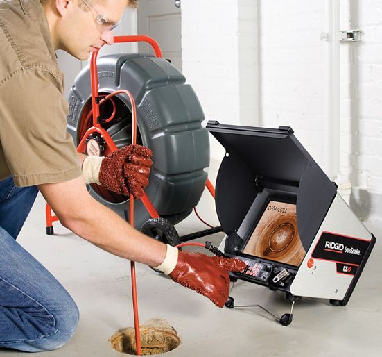 A man is kneeling down in front of a camera that says ridgid on it