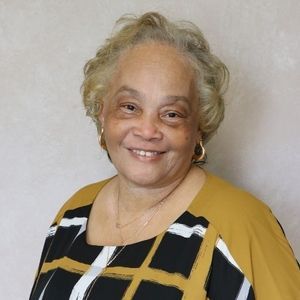 Smiling person in a patterned top, gold and black colors, gold earrings, necklace.