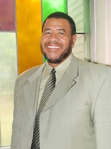 Man in a light suit smiles, standing near a stained glass window.