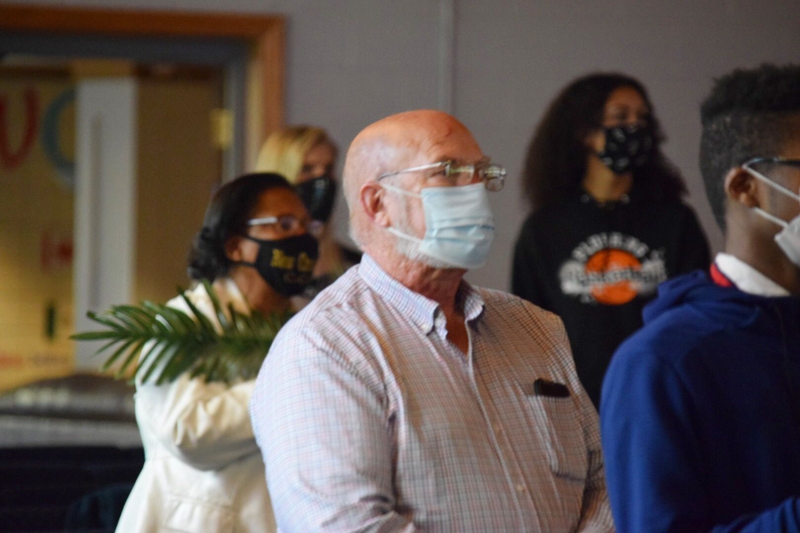 People wearing masks indoors, one holding a palm branch, looking forward.