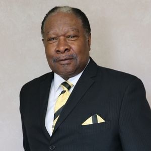 Man in black suit and gold tie, smiling, looking at the camera.