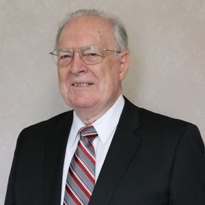 Man in a suit and tie, smiling, wearing glasses.