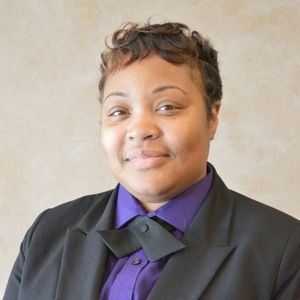 Person wearing a purple shirt, black bow tie, and black blazer, smiling at the camera.