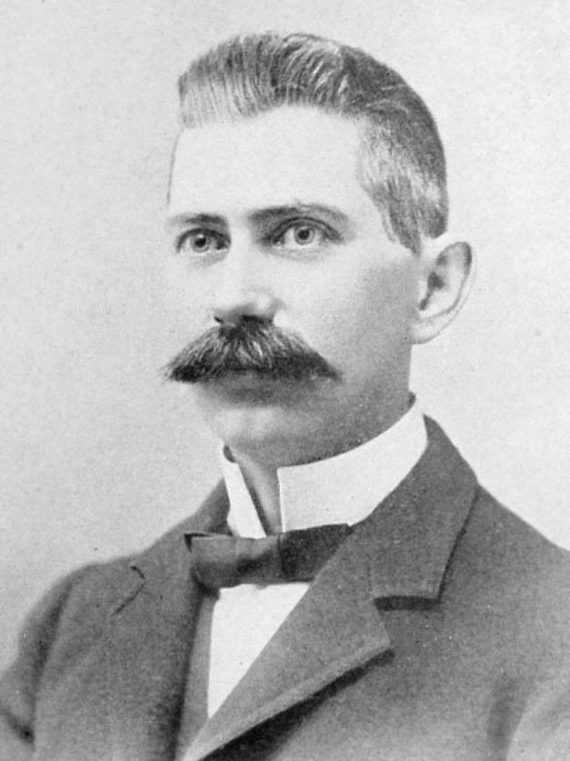 A man with a mustache is wearing a suit and bow tie.