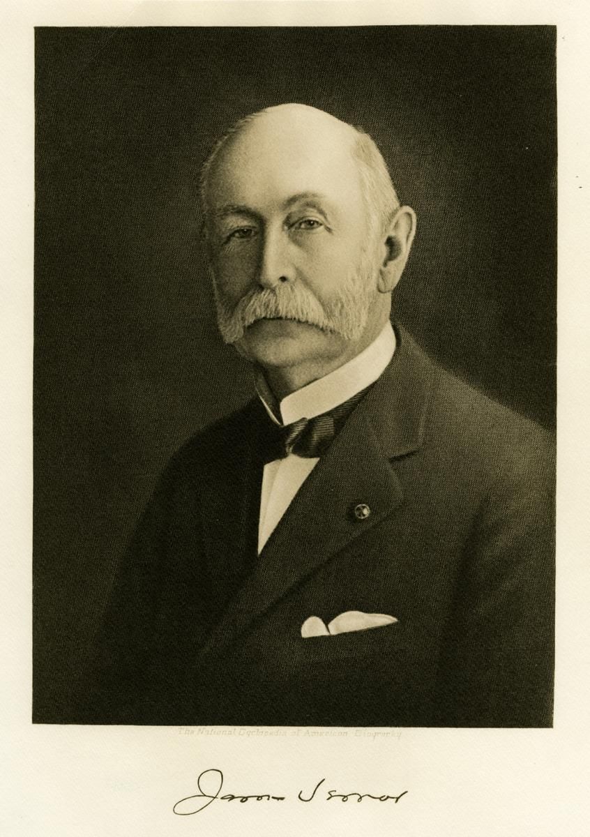 A man with a mustache is wearing a suit and bow tie