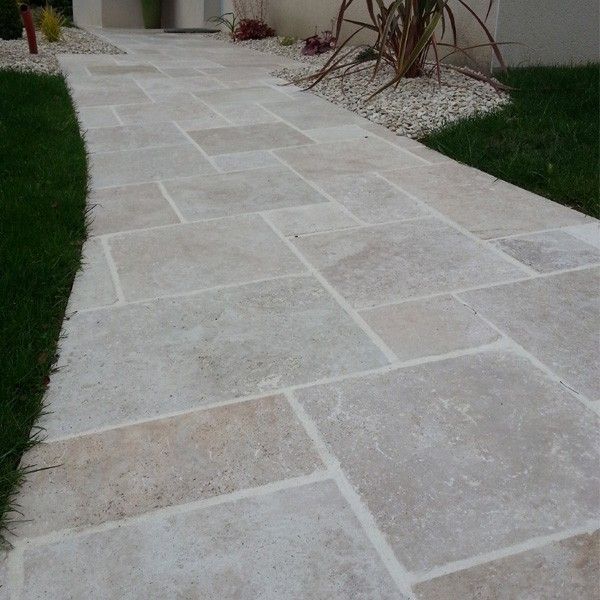 Light gray stone walkway leading through a landscaped garden with grass and shrubs