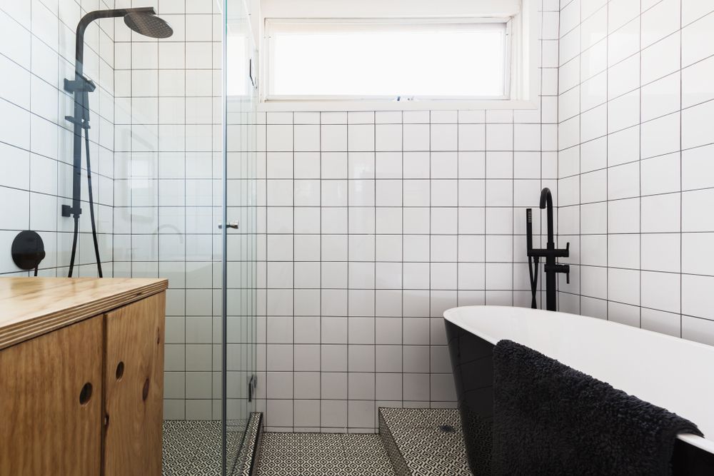 Modern Bathroom With White Tiled Walls, Black Bathtub, and Wooden Vanity — Affordable Tiles and Pavers In Morisset, NSW