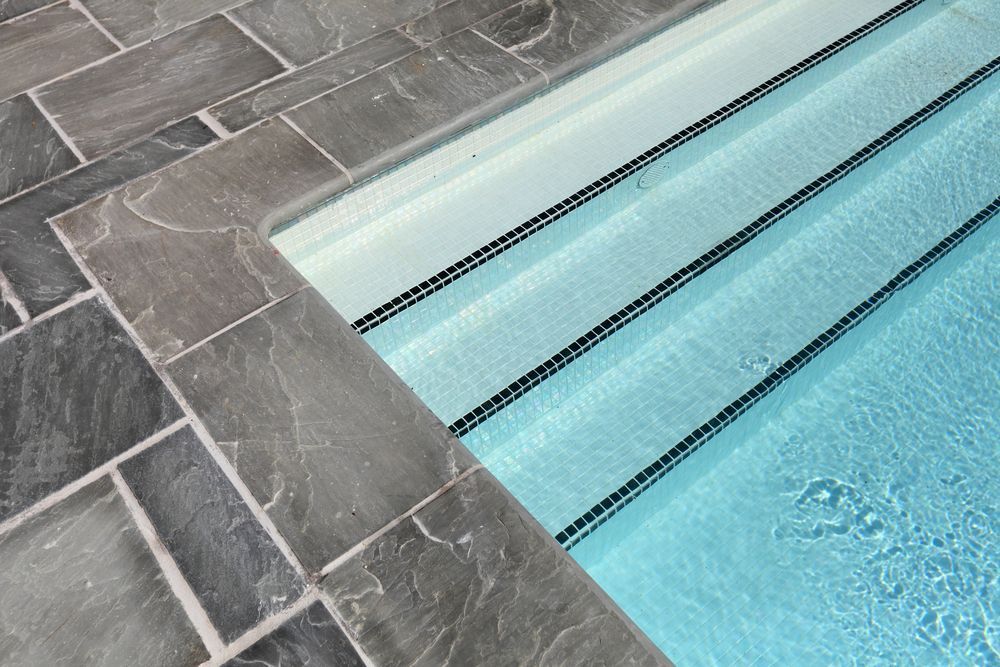 Pool Steps With Blue Water, Surrounded by Gray Stone Tiles — Affordable Tiles and Pavers In Morisset, NSW