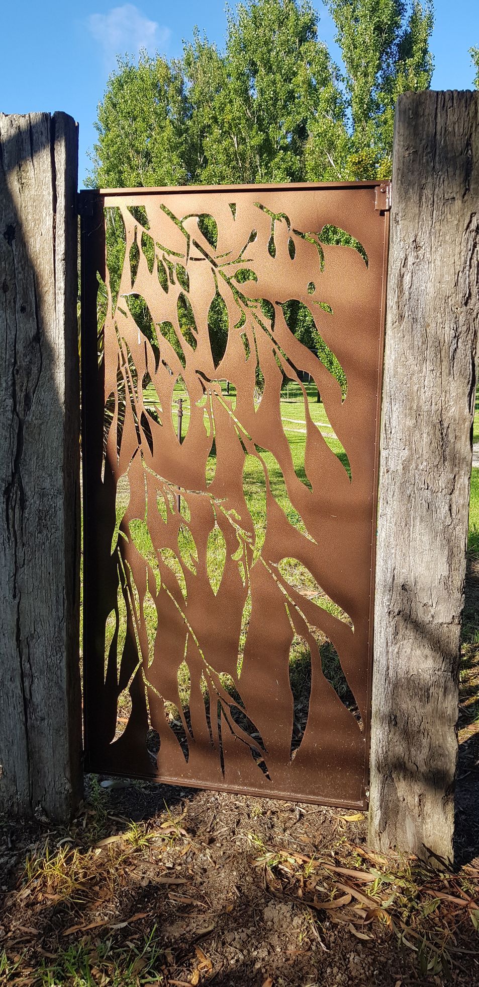A metal gate with leaves on it is surrounded by concrete pillars.