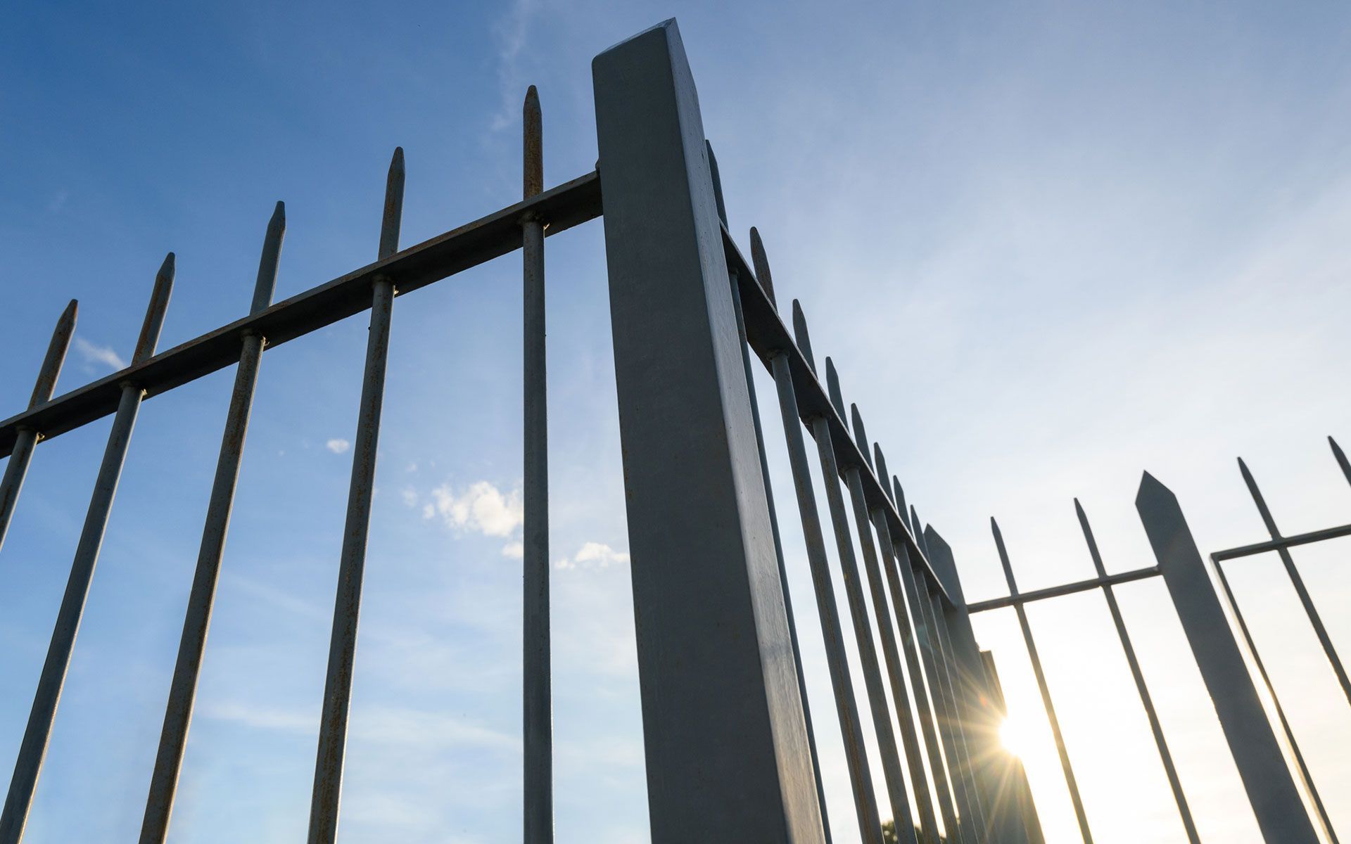 A close up of a metal fence with the sun shining through it.