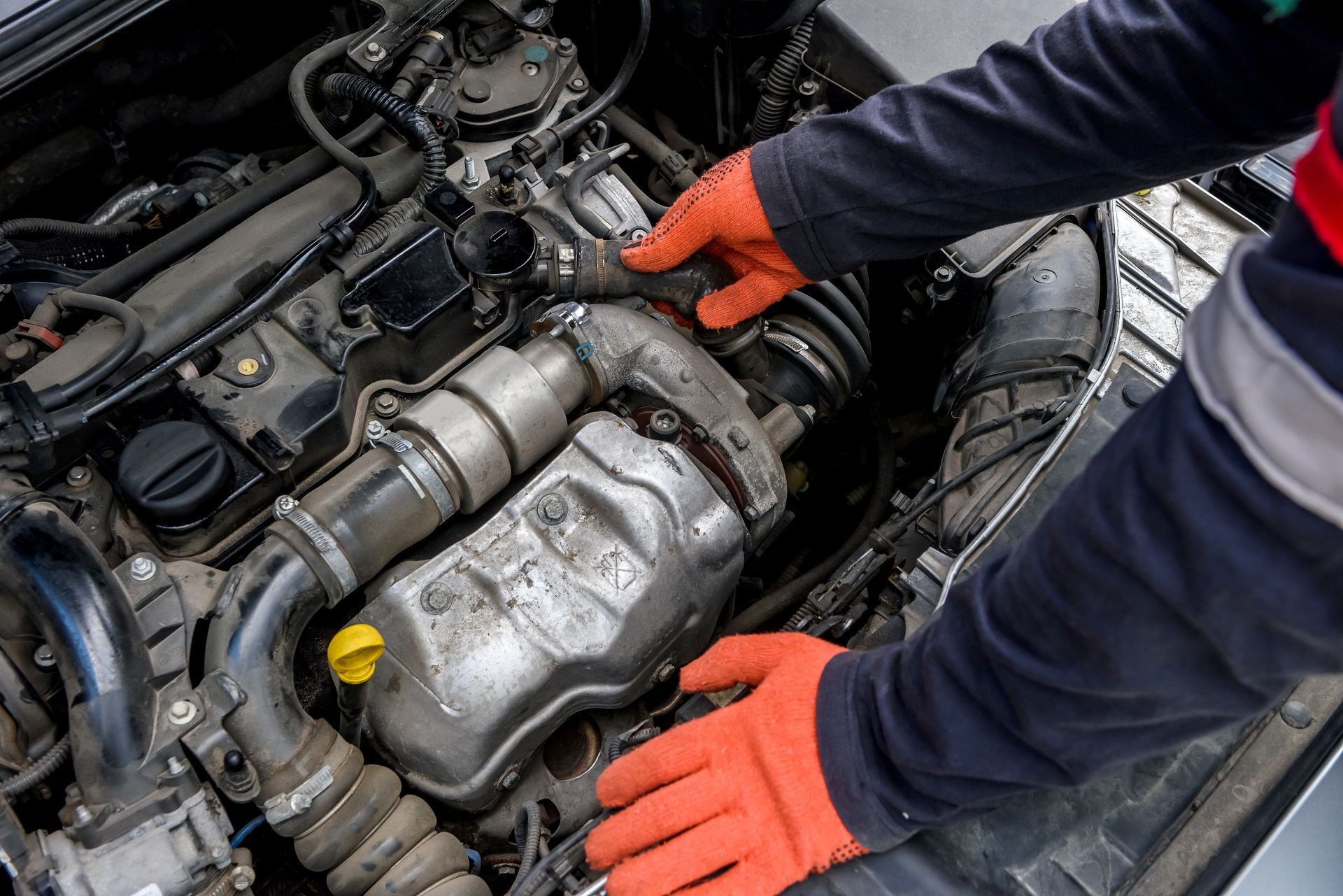Mechanic inspects engine components while wearing bright orange protective gloves. Mechanic inspects engine components while wearing bright orange protective gloves.