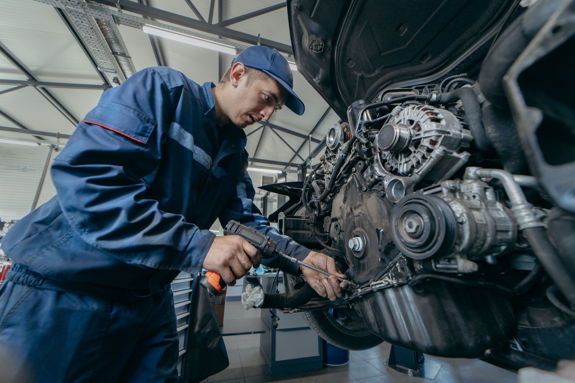 A mechanic in a blue uniform performs engine repair on a car, showcasing his skills in an auto shop.