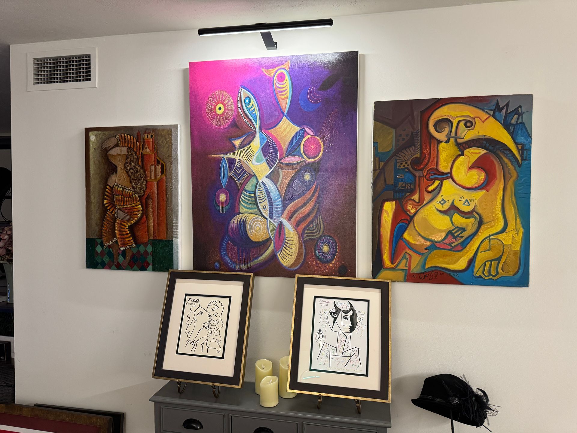 Four framed artworks with a light above; includes a moon landing scene and a Banksy piece, displayed on a wall that was installed in a house in Fairfield County.