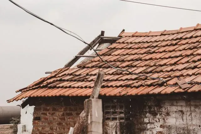 Severely damaged tiled roof with exposed wooden structure requiring roof repair and restoration services.