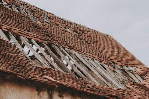 Severely damaged tiled roof with exposed wooden structure requiring roof repair and restoration serv