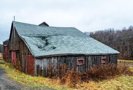 Old barn with severe roof damage and collapsed shingles requiring roof repair and restoration servic