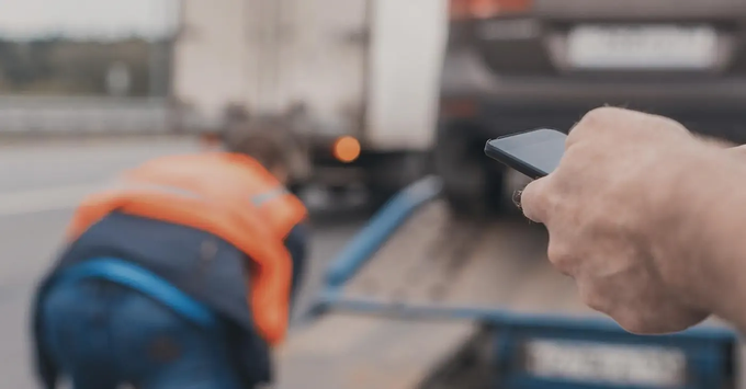 A person is holding a cell phone in front of a tow truck.