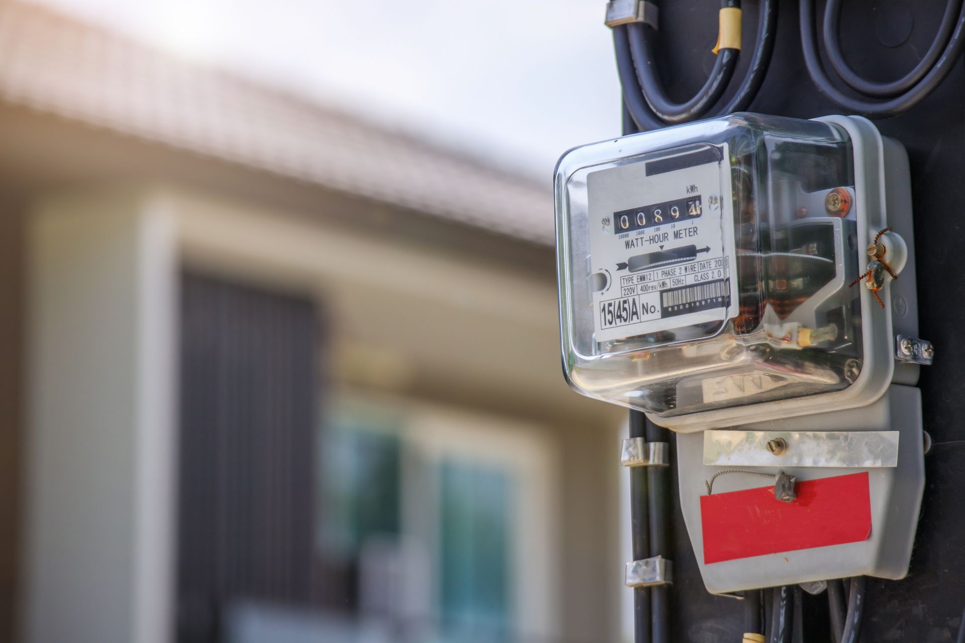 A close up of an electric meter on a pole in front of a house.