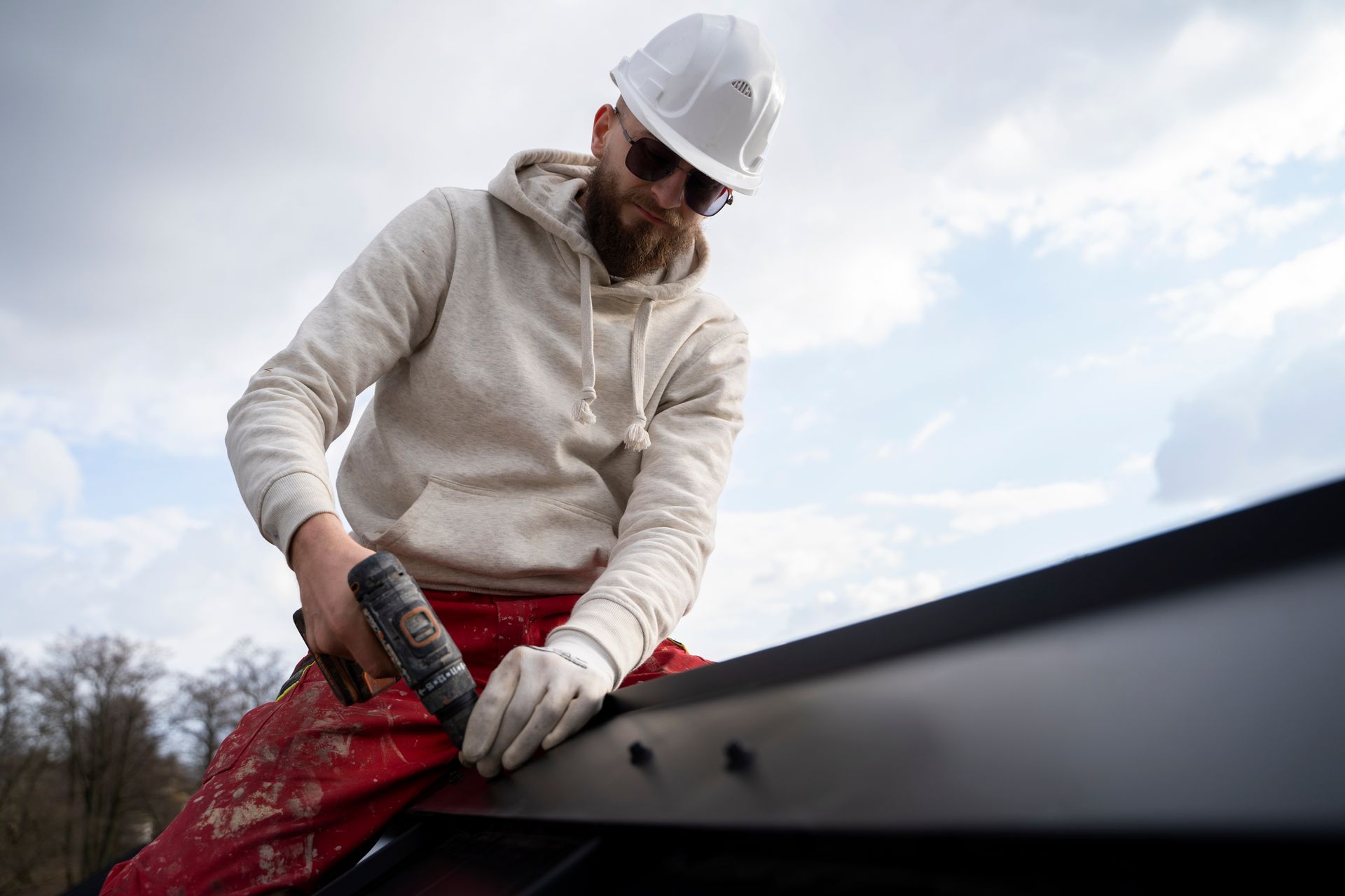 A man wearing a hard hat and sunglasses is working on a roof.