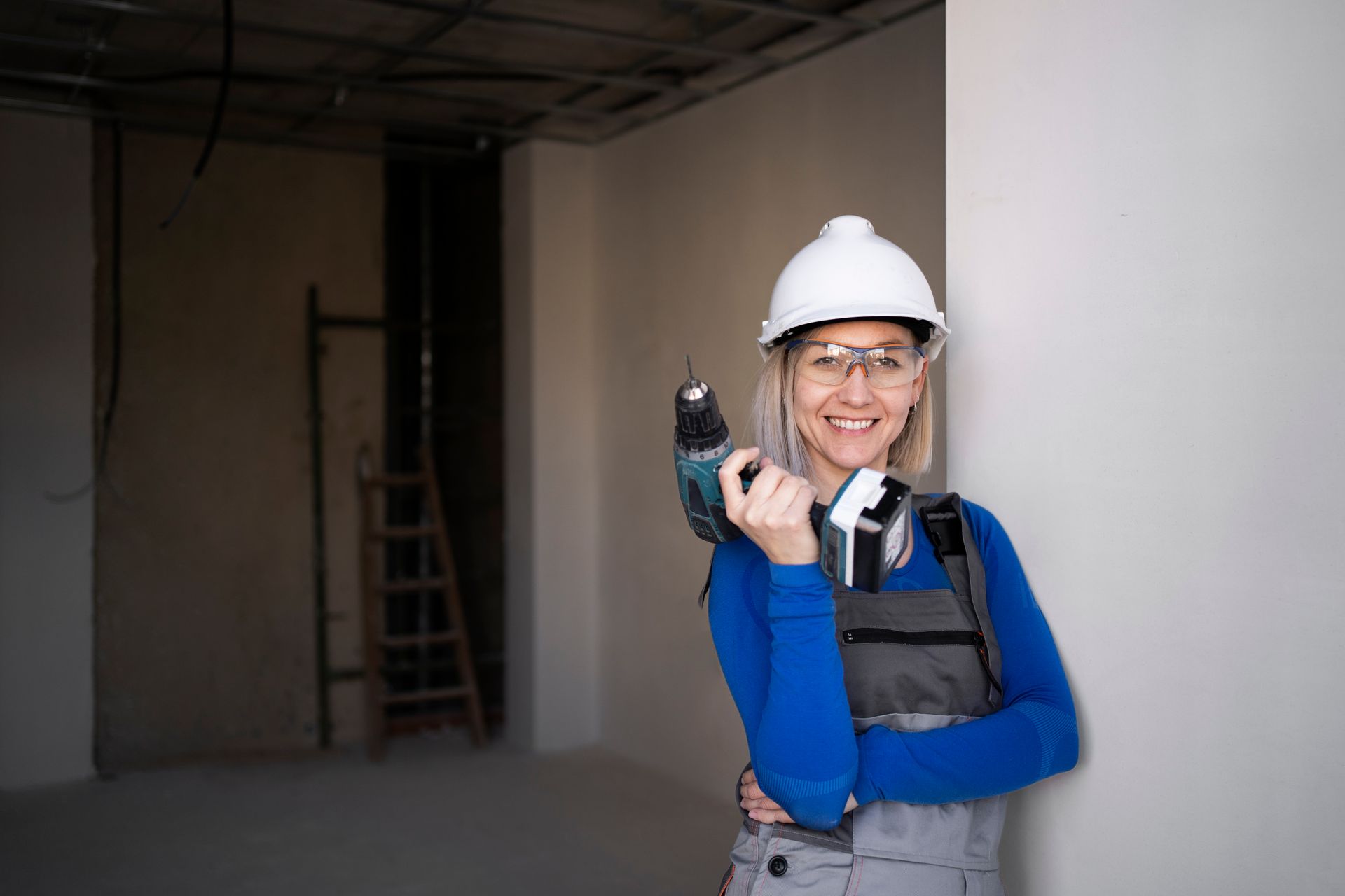 A woman is holding a drill in a room under construction.