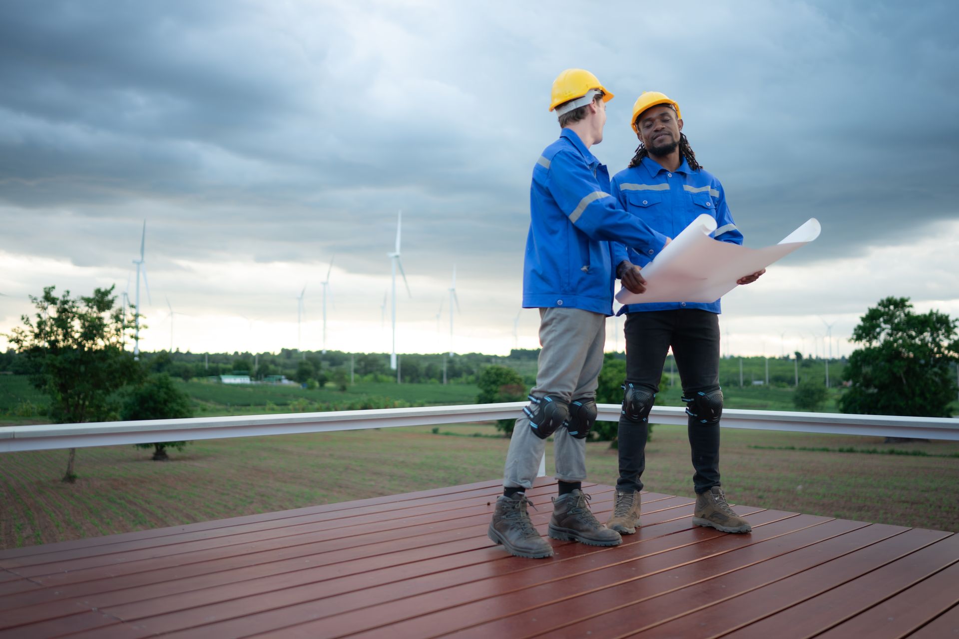 Two construction workers are standing on a deck looking at a blueprint.