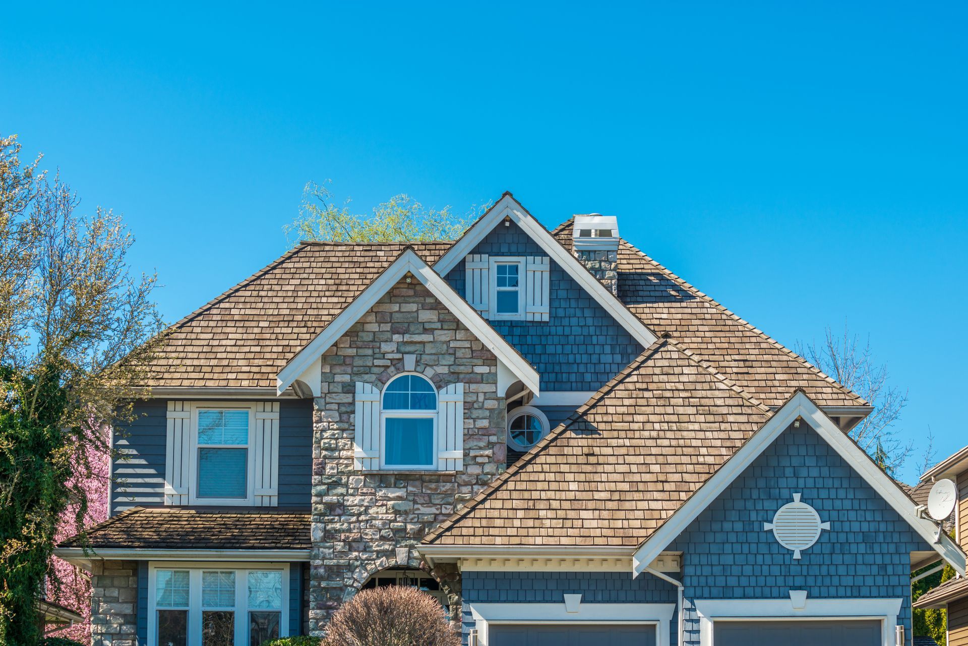 A large house with a shingle roof and a blue sky in the background.