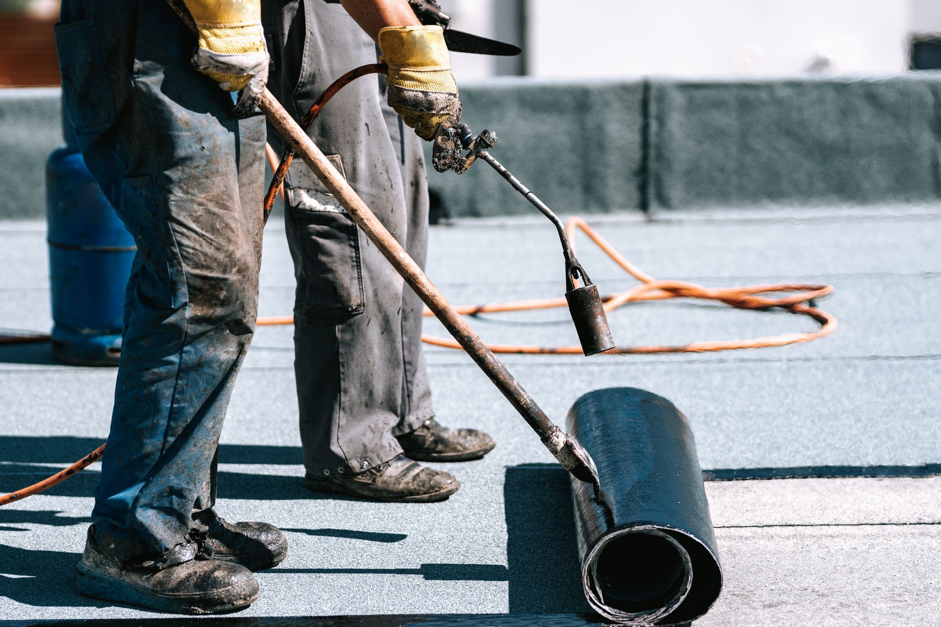 A man is rolling a roll of roofing material on a roof.