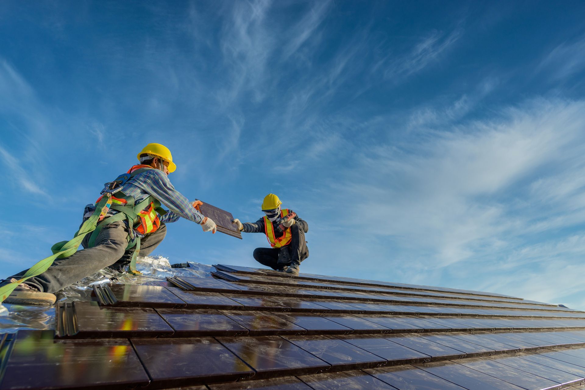 Two construction workers are installing solar panels on a roof.