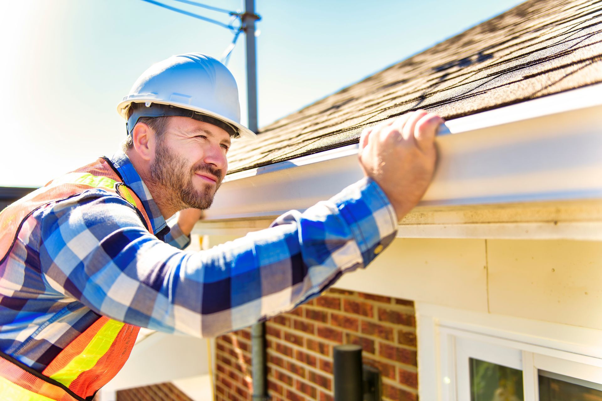 A man is fixing a gutter on the roof of a house.