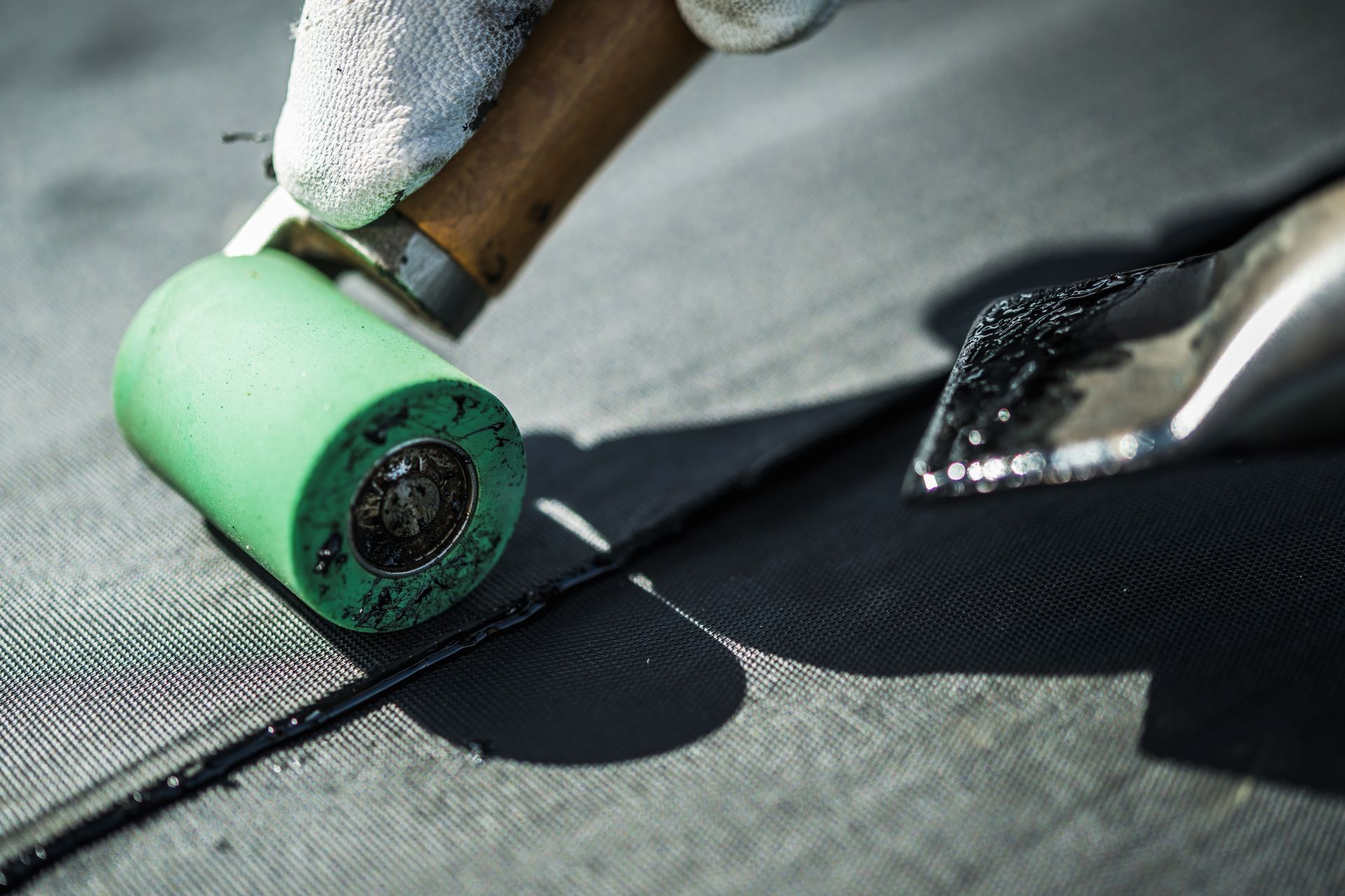 A person is using a green roller on a roof.