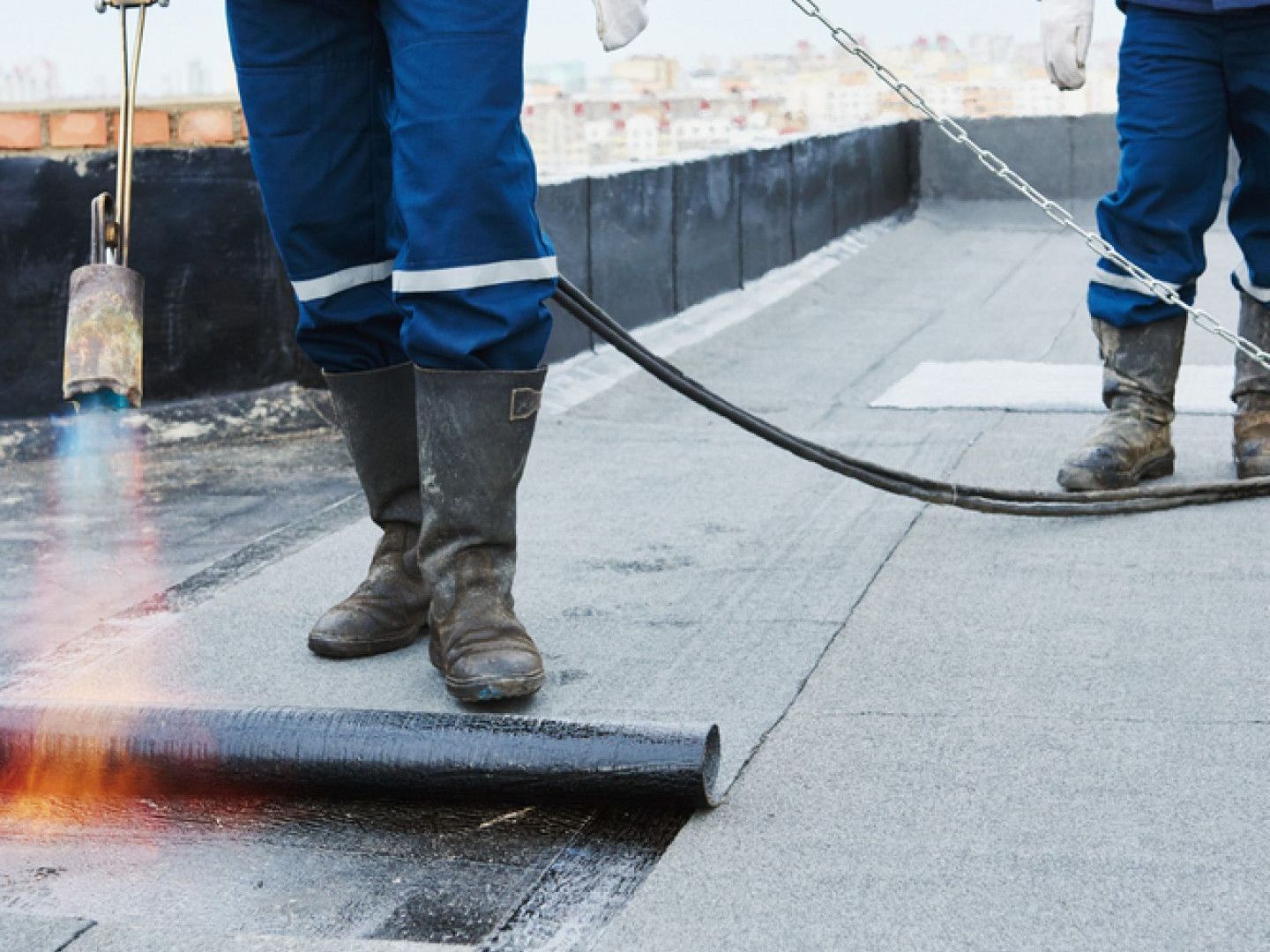 Two men are working on a roof with a torch.