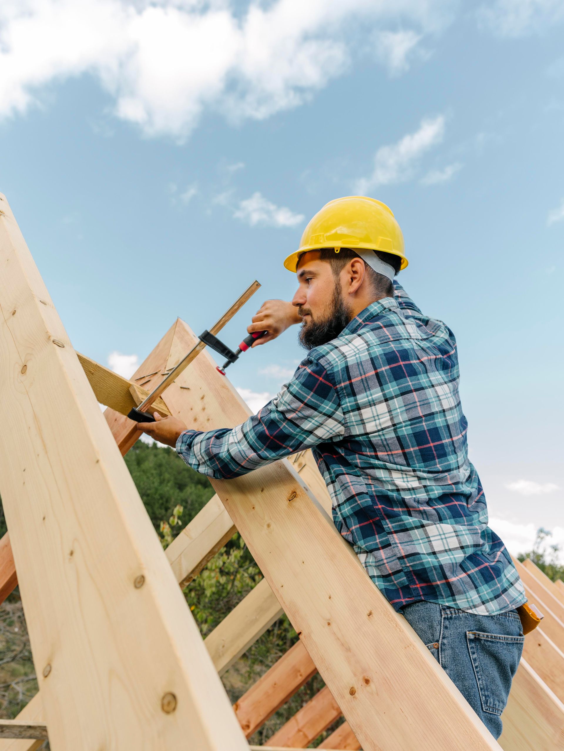 A man wearing a hard hat is working on a wooden structure.