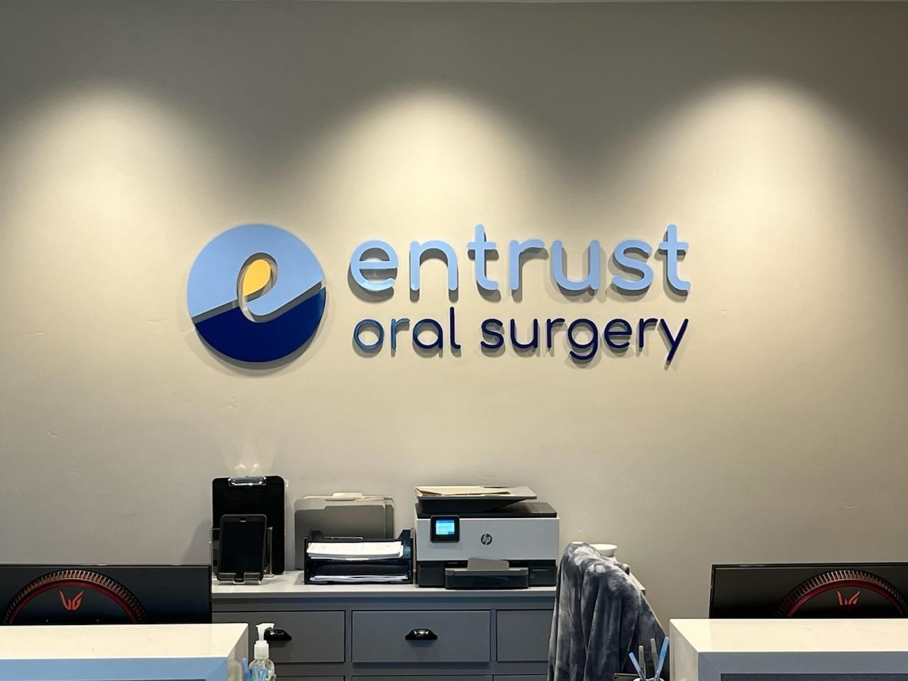A sign for entrust oral surgery is on a wall above a desk.