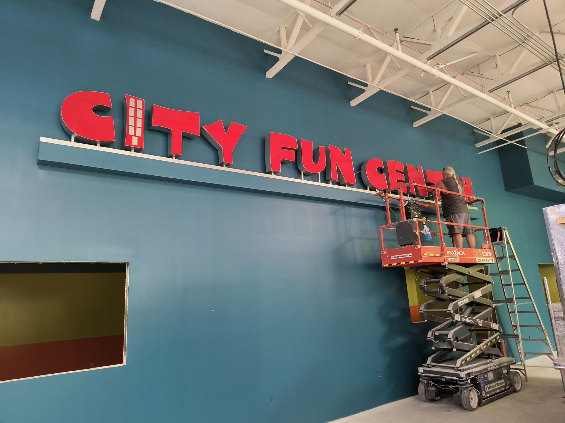 A city fun center sign is being installed on a blue wall.