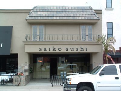 A white truck is parked in front of a building that says saiko sushi