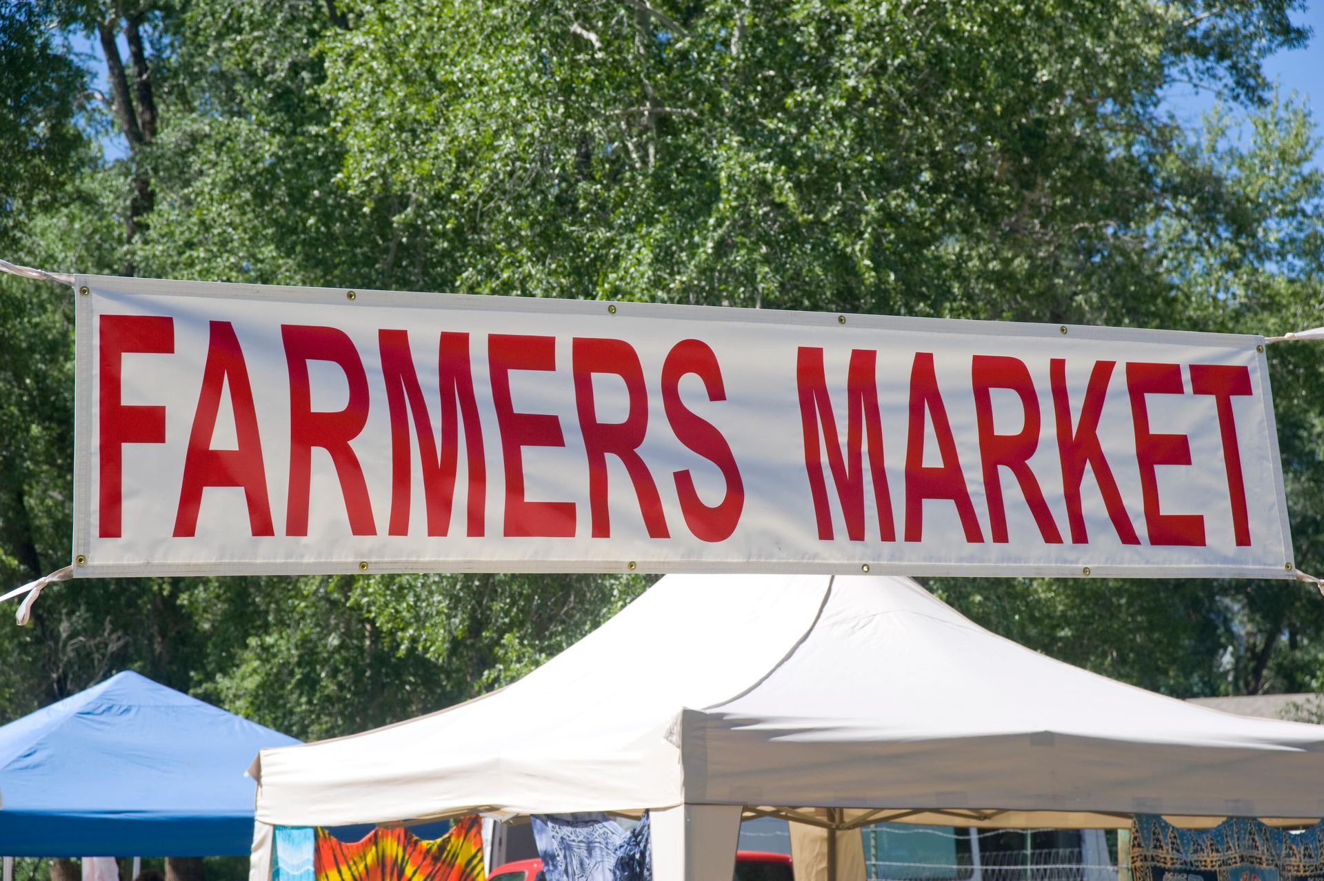 A farmers market sign hangs over a tent