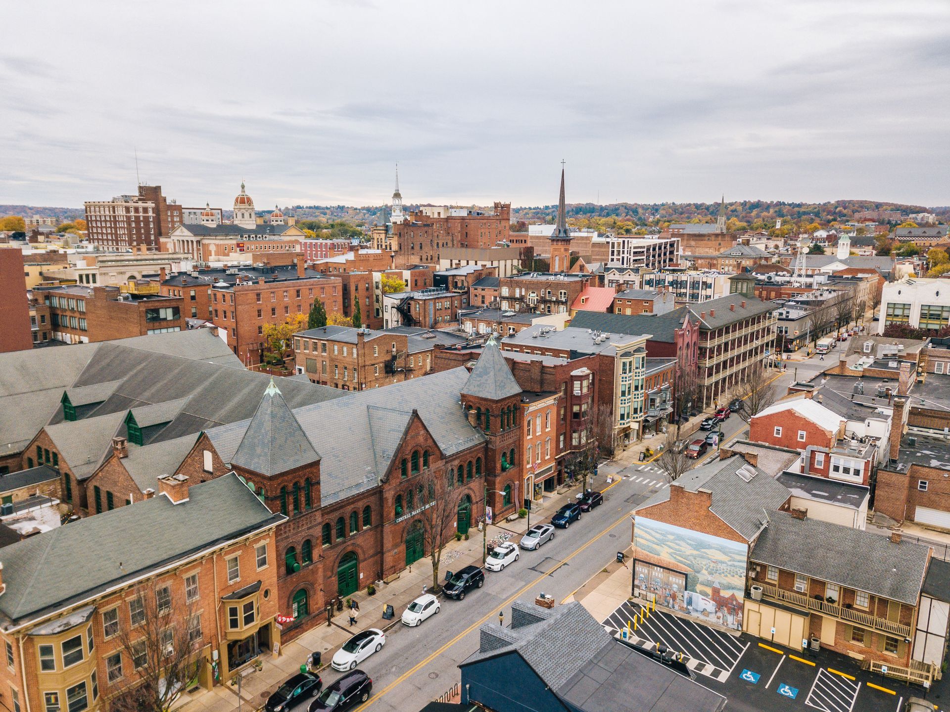 Aerial view of urban cityscape with brick buildings, road, and parked cars under an overcast sky.