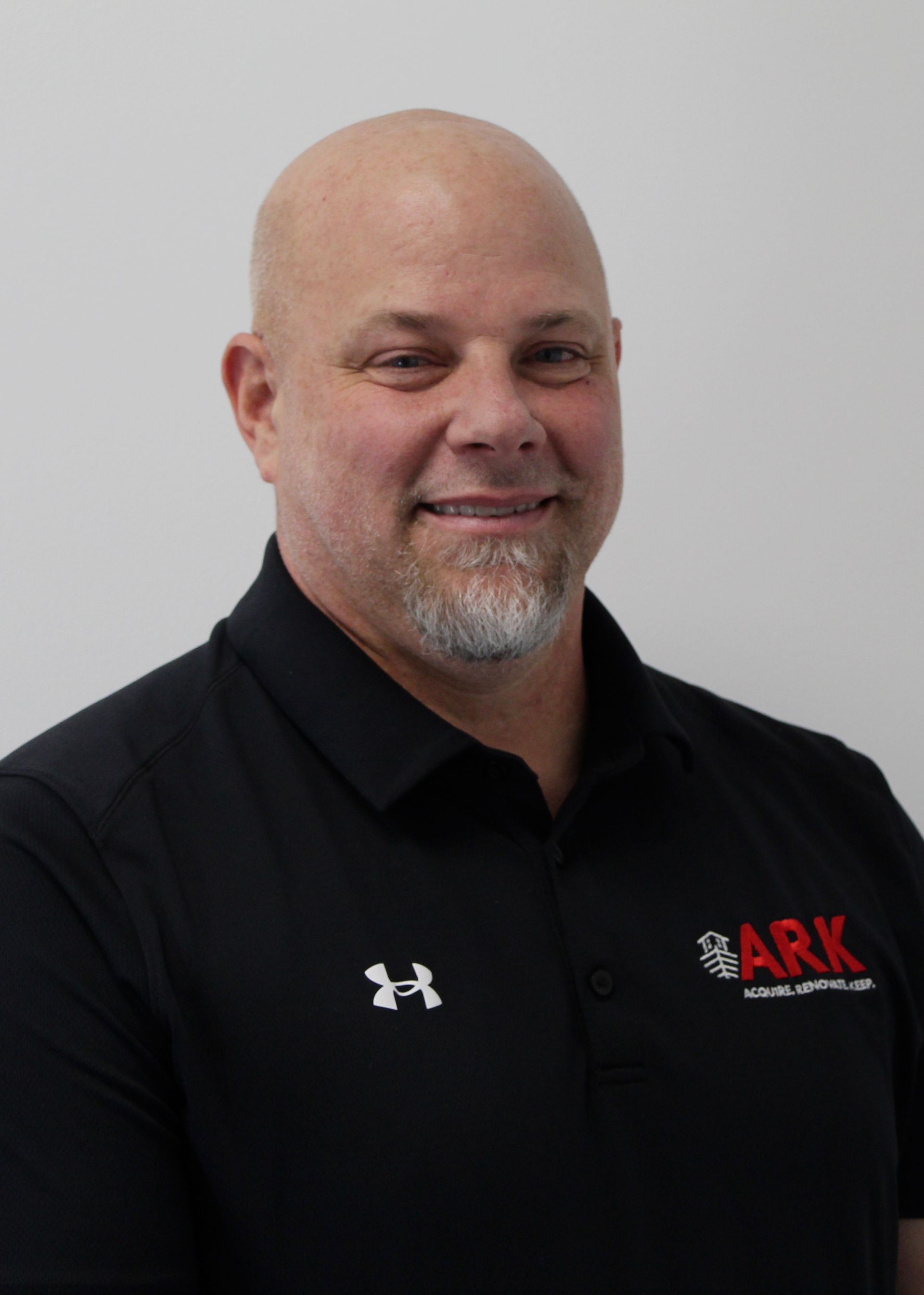 Bald man with goatee wearing a black polo shirt with 