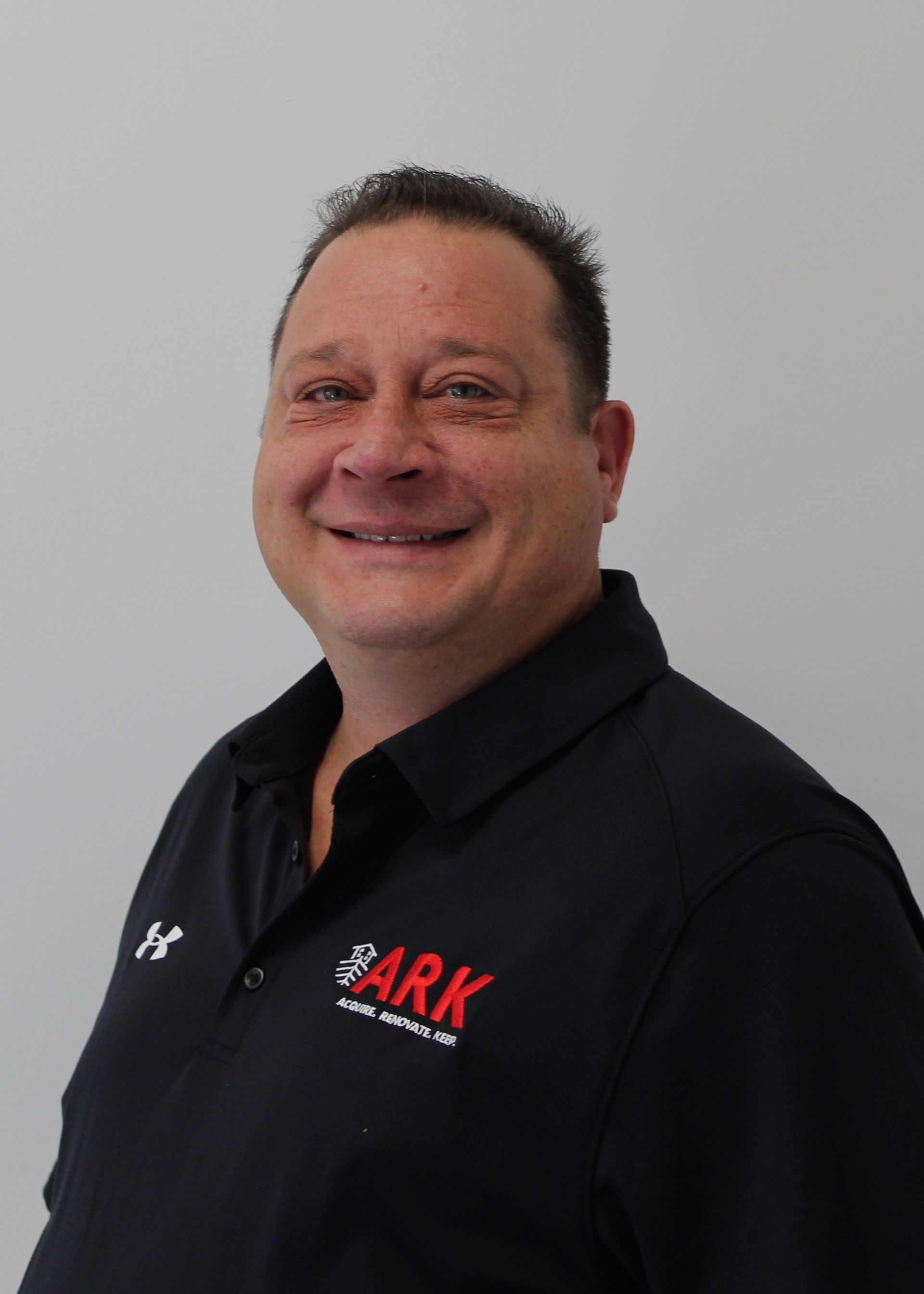 Man wearing a black polo shirt with ARK logo, smiling at the camera.