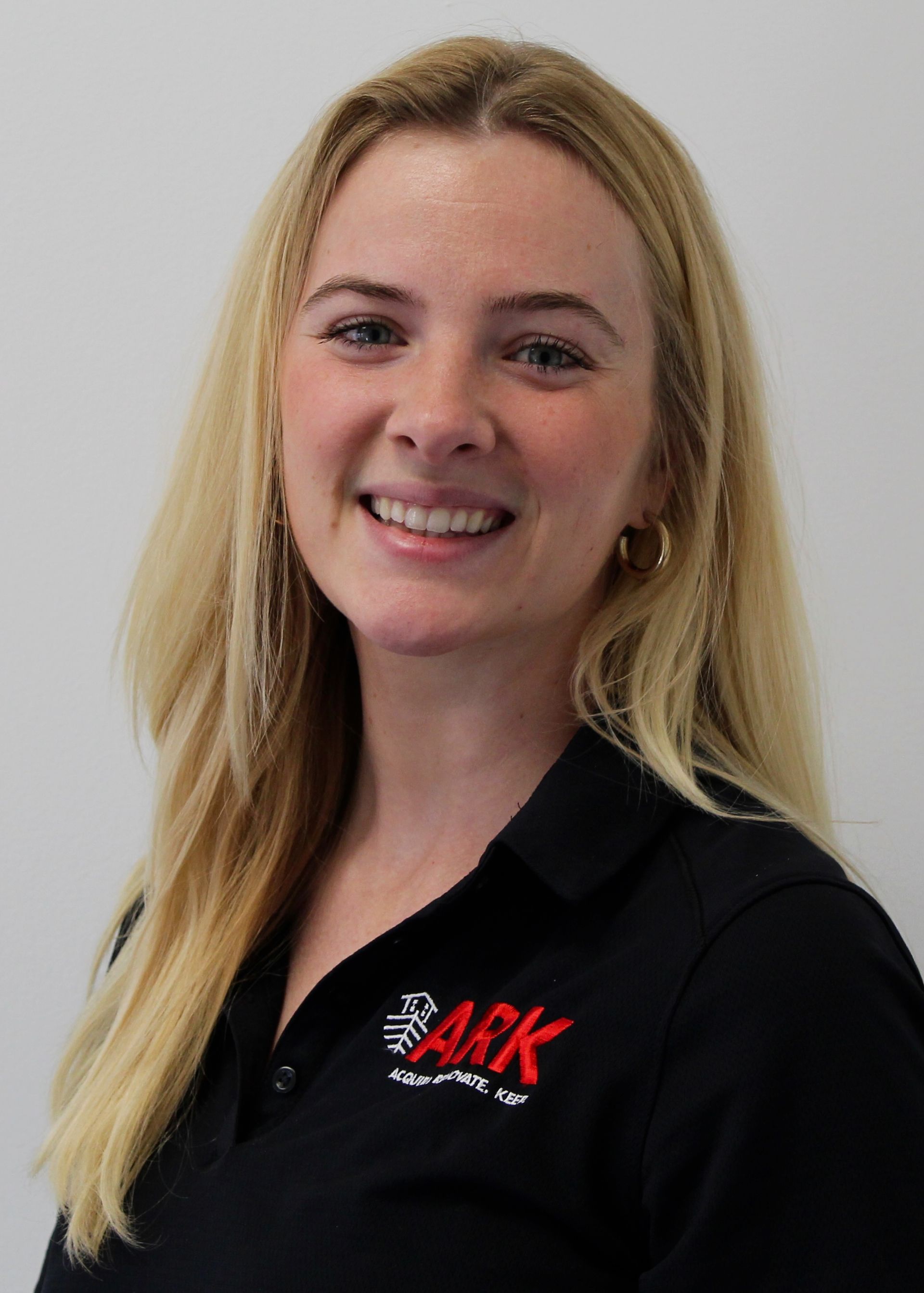 Blonde woman smiling, wearing a black shirt with a logo, against a white background.