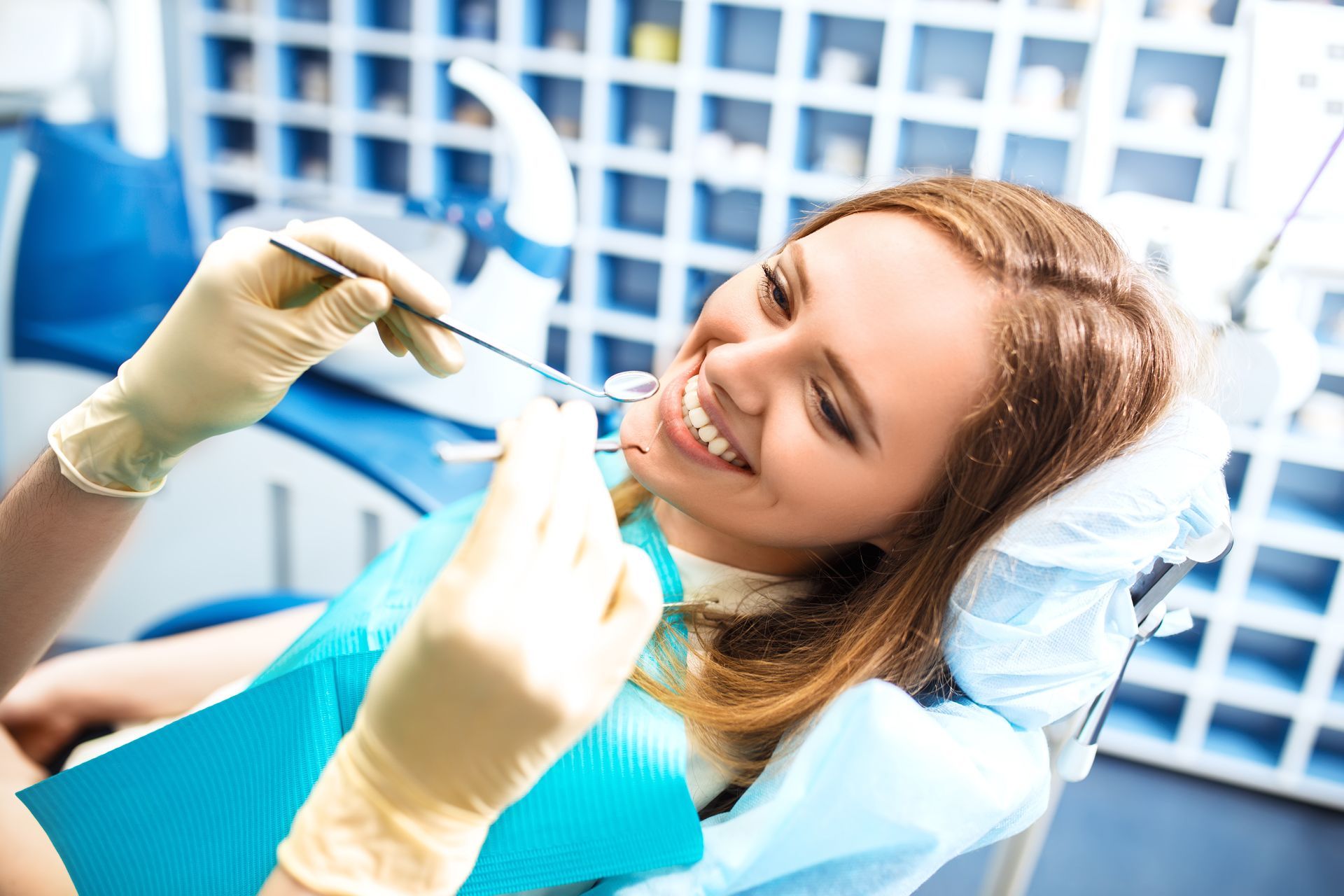 Patient smiling in a dental chair while dentist holds a dental mirror and tool during an exam