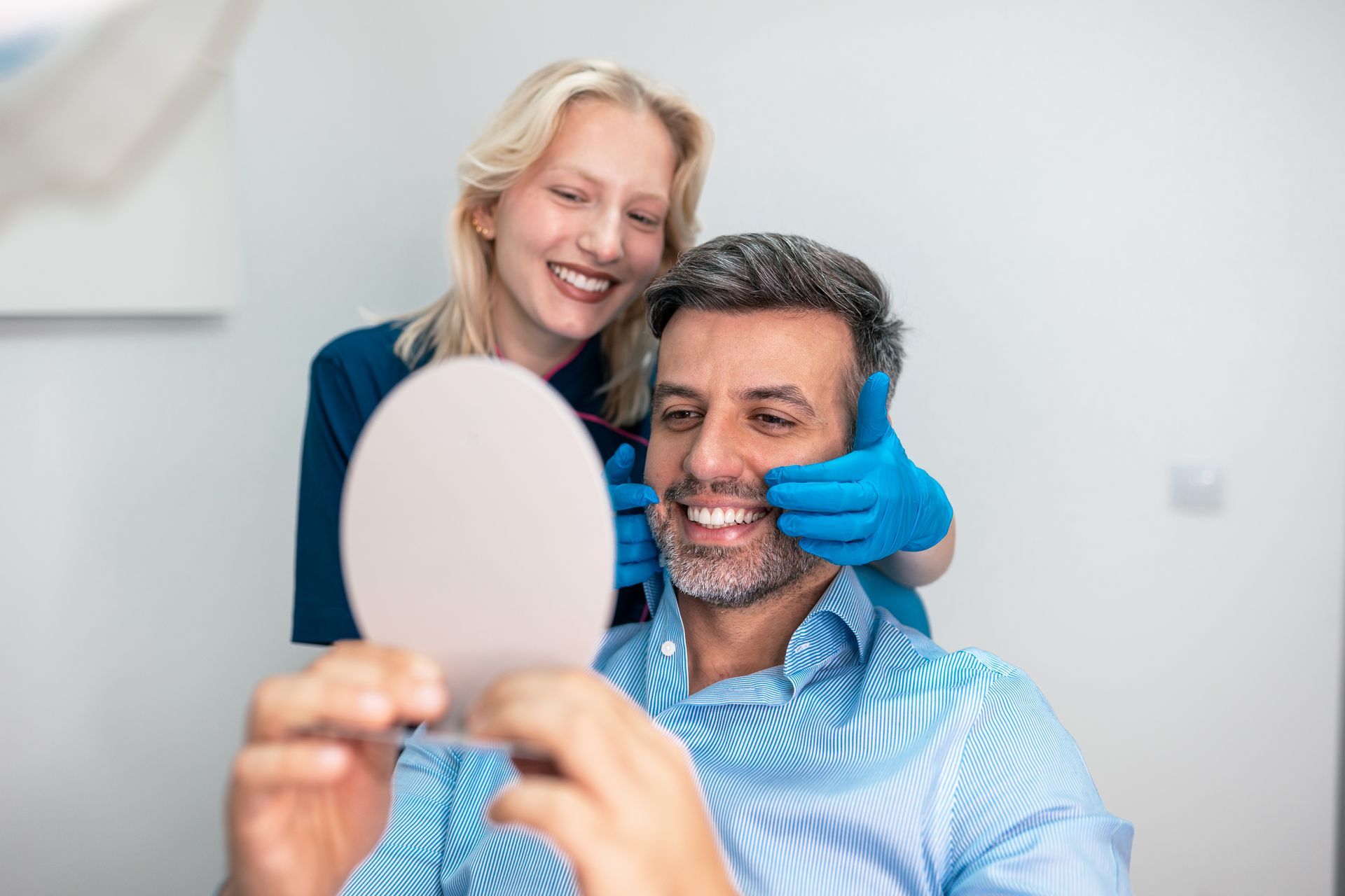 Smiling dentist examining a man’s teeth with a mirror in a bright clinic
