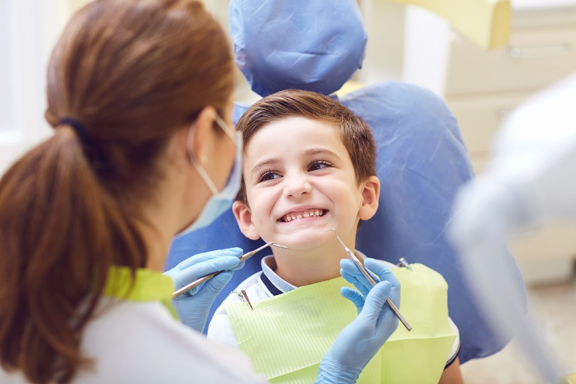 Dentist examining a smiling child’s teeth with a dental mirror and gloves