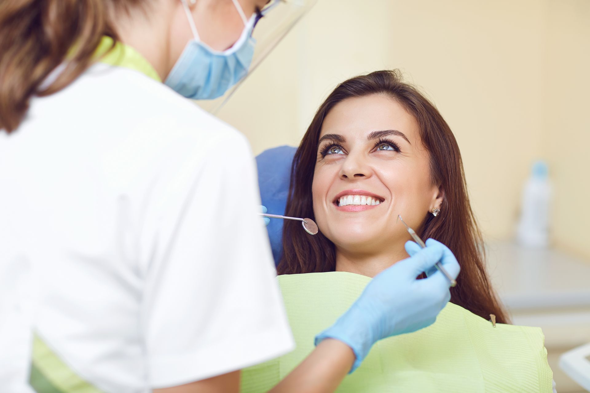Dental patient smiling while dentist examines her teeth with a mirror and gloved hands