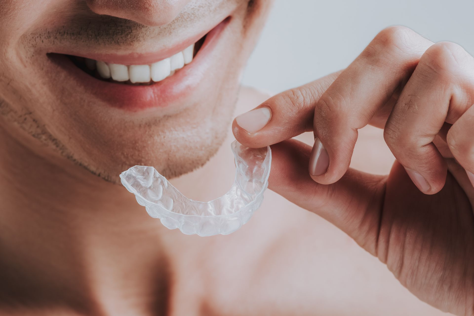 Person holding a clear dental aligner near their smiling mouth
