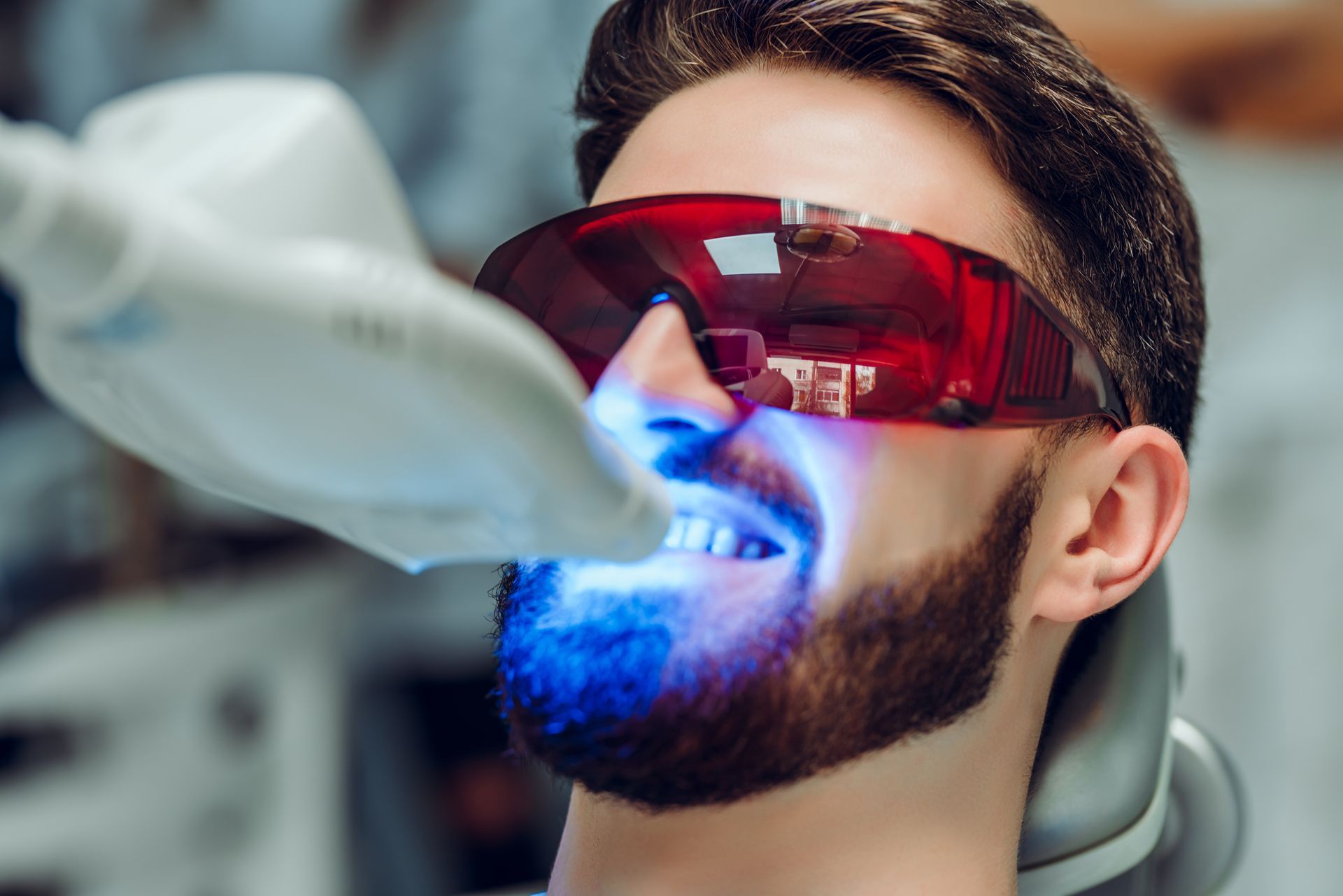 Person wearing red protective goggles and a beard during a blue light dental procedure