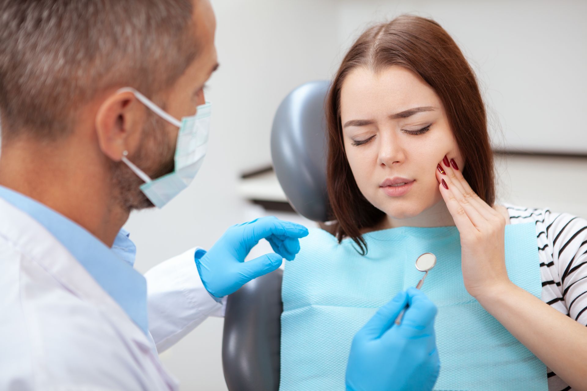 Dentist examining a patient’s tooth as she holds her cheek in a dental chair