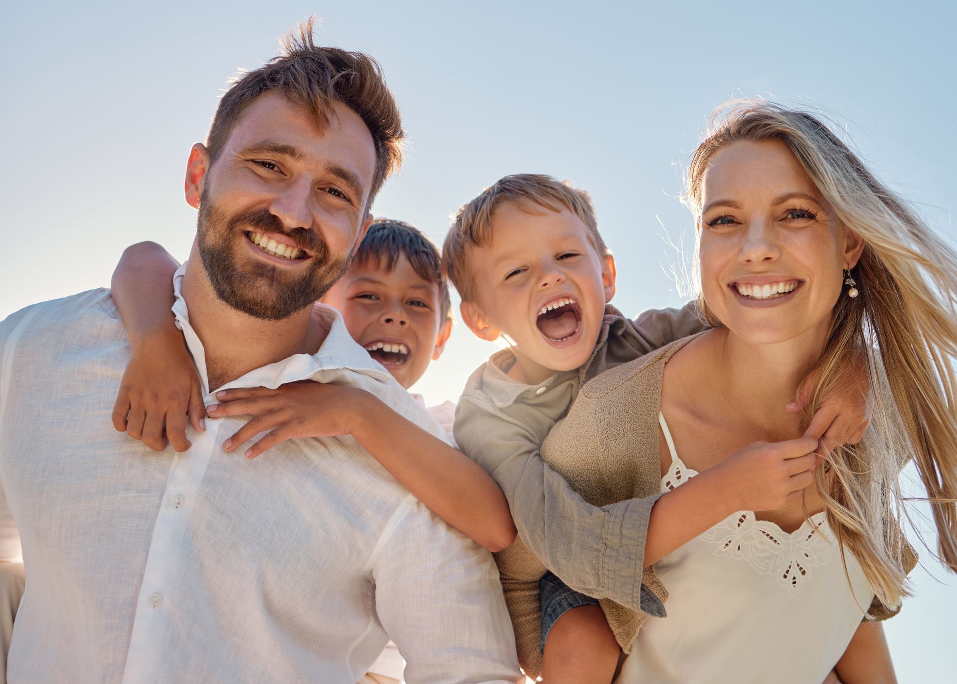 Family smiling together on a sunny beach, with children on their parents’ backs.